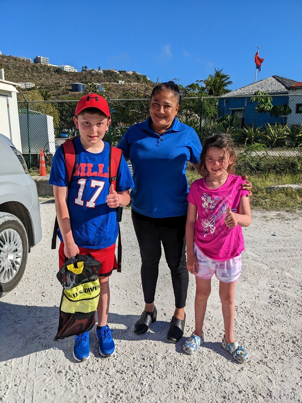 A Sunita Tours guide smiling with two young guests beside the tour van in St. Maarten