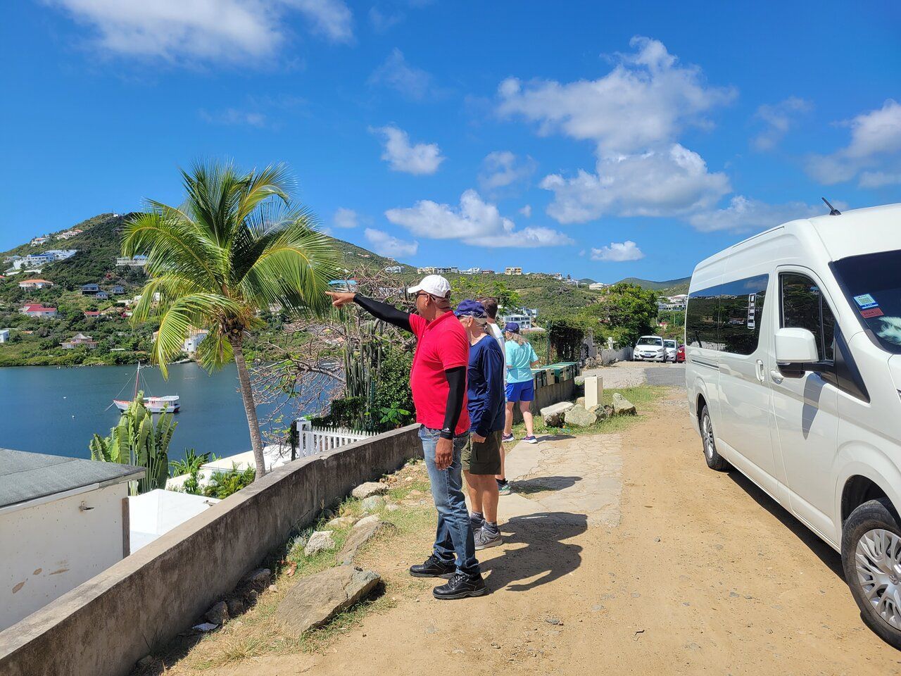 Sunita Tours guide pointing out the view to guests at a hillside lookout in St. Maarten, with the tour van parked nearby
